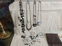 View of all costume jewelry laid out on a white cloth backdrop including necklaces, earrings, bracelets, and brooches.