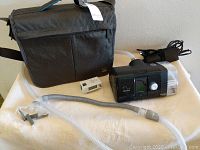 ResMed AirCurve 10 BiPAP machine with accompanying travel bag, wall timer, and tubing laid out on a beige surface.
