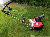 Photo of the Toro electric snowblower from a side angle showing the handle, body, wheels, and chute with extension cords wrapped at the base.