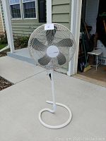Full view of white Holmes standing fan with circular base outdoors.