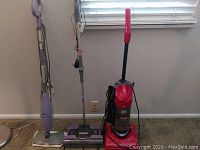 Three vacuum and floor cleaning units displayed including Dirt Devil upright vacuum, Shark cordless vacuum, and Shark floor cleaner.