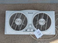 White Duracraft dual fan window unit on carpet with control knobs and power cord visible.