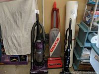Photo showing three upright vacuum cleaners side by side and the rolled white wall vinyl sheet.
