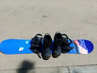 Full set photo showing blue K2 snowboard with attached black bindings and pair of black Lamar boots beside it.