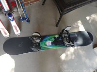 Top view of the snowboard lying on concrete floor showing colorful top graphic and black bindings.