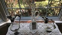 Three decanters on a white lace runner by a window, varying heights visible, 17 inch, 13 inch, and 10 inch as described by seller