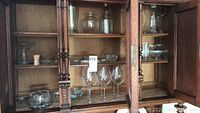 Glass cabinet with shelves holding crystal and glassware including wine glasses, decanter, bowls and trays