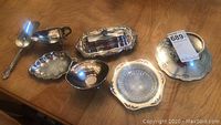 Overview of eight assorted silverplate serving pieces laid out on wood table