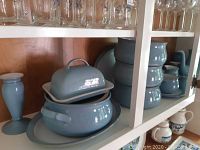 Photo of several serving pieces on a shelf including lidded pot, stack of bowls, and a vase