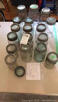 Photo showing a collection of approximately 17 vintage and antique Mason jars of varying sizes and colors, mostly clear glass with some light tints, all with zinc lids.