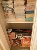 Closet shelf showing three stacks of folded towels above boxed ladder
