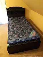 Full view of single bed with headboard, mattress, and under-bed drawers against a yellow wall with slanted ceiling.