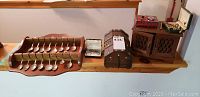 Wide shot of a wooden rack holding 13 metal collectible souvenir spoons, a small open jewellery box with pearl necklace, a wooden jewellery chest with metal accents, and a lattice-design wooden jewellery box.