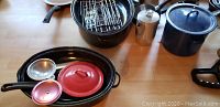 Top view showing black enamel roasting pan with rack inside, red and silver pots, and other items