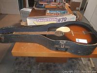 Full side view of the vintage Kay acoustic guitar in hard case placed on a table.