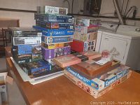 Stack of assorted jigsaw puzzle boxes and boxed games piled on a table.