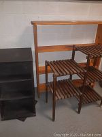 Photo showing the three storage shelves including the black swivel unit, tiered wooden shelf, and pine wood shelf against a cinderblock wall.