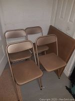 Four brown metallic Samsonite folding chairs and matching folding card table leaning against wall