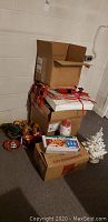 Stack of cardboard boxes containing Christmas decorations with some items out in front including a ceramic Christmas tree and light boxes.