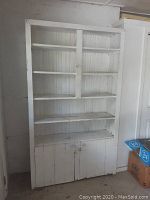 Front view of vintage white wooden cupboard showing five upper shelves and two-door lower storage cabinet.