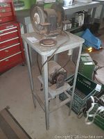 Full view of the six inch bench grinder placed on a tall gray metal stand, showing the grinder from an angle with the electrical cord visible.