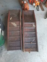 Top-down view of two rusty, metal car ramps with visible dirt and oil stains.