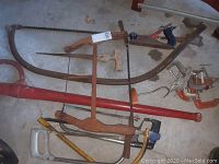 Vintage wooden frame Swede saws and other hand saws plus clamps and a hand planer laid on concrete floor