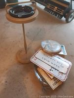 Floor ashtray and pile of metal signs and decorations on concrete floor.