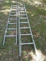 Two aluminum ladder components lying on grass, visible wear and damage, one hinge damaged