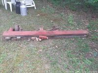 Overall view of red-painted wood lathe bed with headstock and tailstock assemblies laid on grass