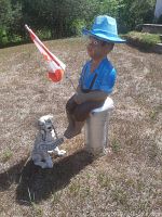 Boy sitting on metal post holding Canadian flag with dog ornament beside it on dry grass