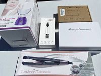 Wide shot showing all items in the lot including the facial steamer, electric blackhead remover, hair straightener, vanity mirror lights, and beauty instrument box.