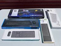 Lot of six computer keyboards and accessories, including wireless and wired models in original packaging on a table