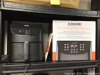 Photo of COSORI air fryer beside its original packaging showing the unit and box design.