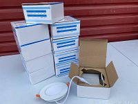 Ten white and blue retail boxes stacked on a table with one open showing a round LED panel light connected to a power driver.