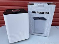 White and black air purifier with control panel on top, shown with packaging box