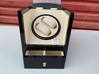 Photo of the black glossy wooden watch winder box with its lid open showing the two watch holders and inner drawer compartment.
