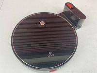 Top view of robot vacuum showing glossy finish and Lefant logo, charging dock visible behind