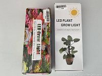 Two plant grow light boxes, one floral patterned and one white with potted plant image, standing upright on a surface.