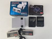 Mini retro gaming console, two wired controllers, two handheld consoles, and their boxes on a white table.