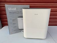Photo of Levoit air purifier with box, showing front and top design, white body with grey top grill.