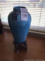 Side view of blue ceramic vase on wooden stand showing dripping paint effect and visible chips/nicks.