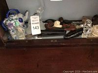 Wide view showing ceramic teapot, glass bottles, several tobacco pipes and pipe cases on a glass tabletop.