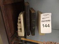 Shelf containing cream ceramic bookends and two vintage hardcover books