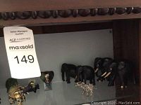 Shelf display with several miniature elephant figurines of various materials and sizes