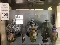 Photo showing front view of all eight miniature oriental style vases arranged in a glass cabinet, highlighting the detailed floral patterns and various colors.