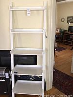 Full view of the white ladder style bookshelf with four shelves leaning against the wall.