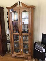 Full view of the tall solid wood curio cabinet showing double glass doors, shelving inside, and overall style.