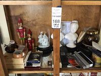 Shelf showing Pinocchio figurines, Christmas dome, ceramic busts, pens and other small items