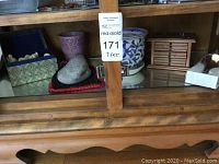 Wooden cabinet glass shelf with various decorative items including a decorative box, ceramic planter, wooden jewelry box, and spoons.